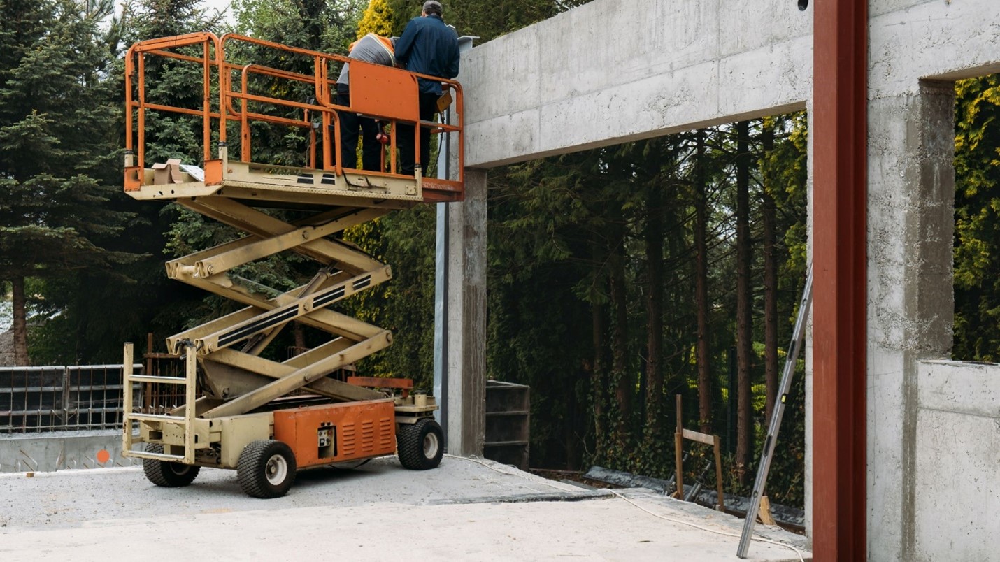A man on a morn scissor lift in front of a building, working on maintenance tasks.