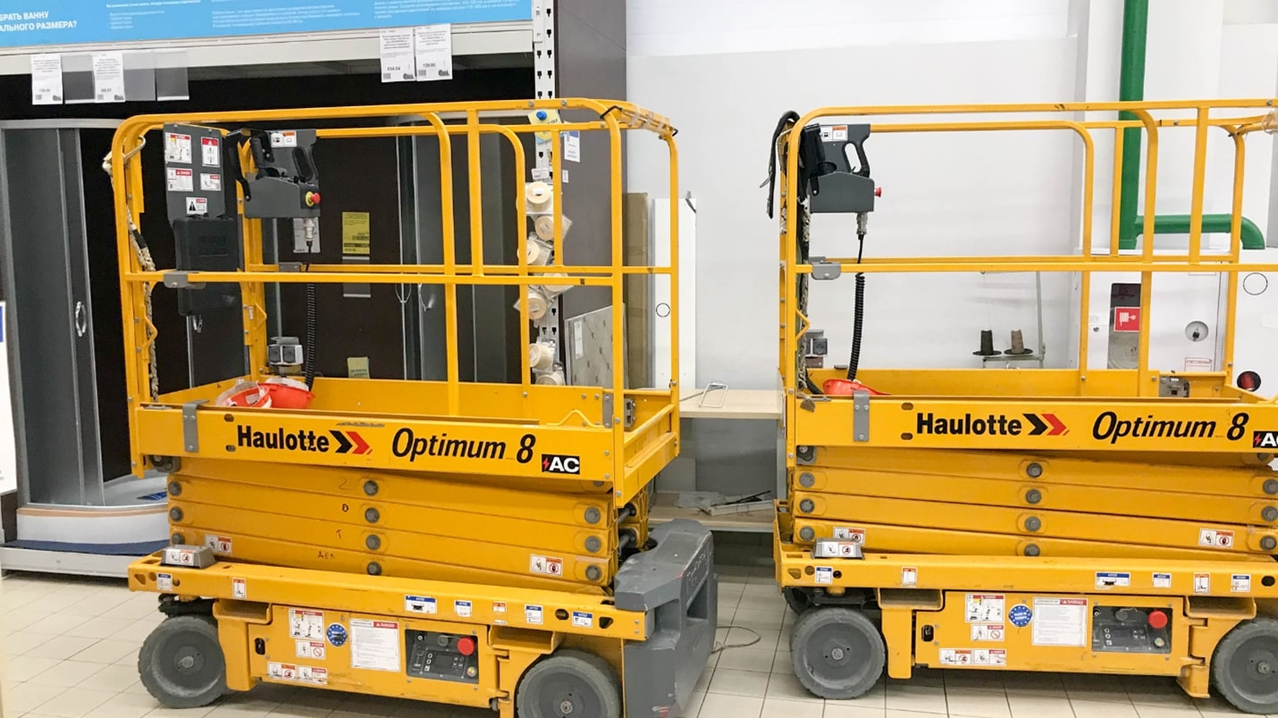 Two yellow Morn scissor lifts in a room with a door.